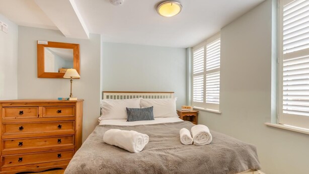 A bedroom with a bed, a wooden dresser, a nightstand, a lamp, and a window with blinds. - 3 Bed in Whitby (oc-w957) (Whitby)