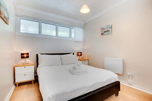 Ein ordentlich eingerichtetes Schlafzimmer mit einem Bett, zwei Nachttischen, einem Fenster mit Jalousien, einer Wandheizung und einem Bild.