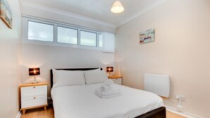 Een netjes ingerichte slaapkamer met een bed, twee nachtkastjes, een raam met zonwering, een wandradiator en een schilderij.