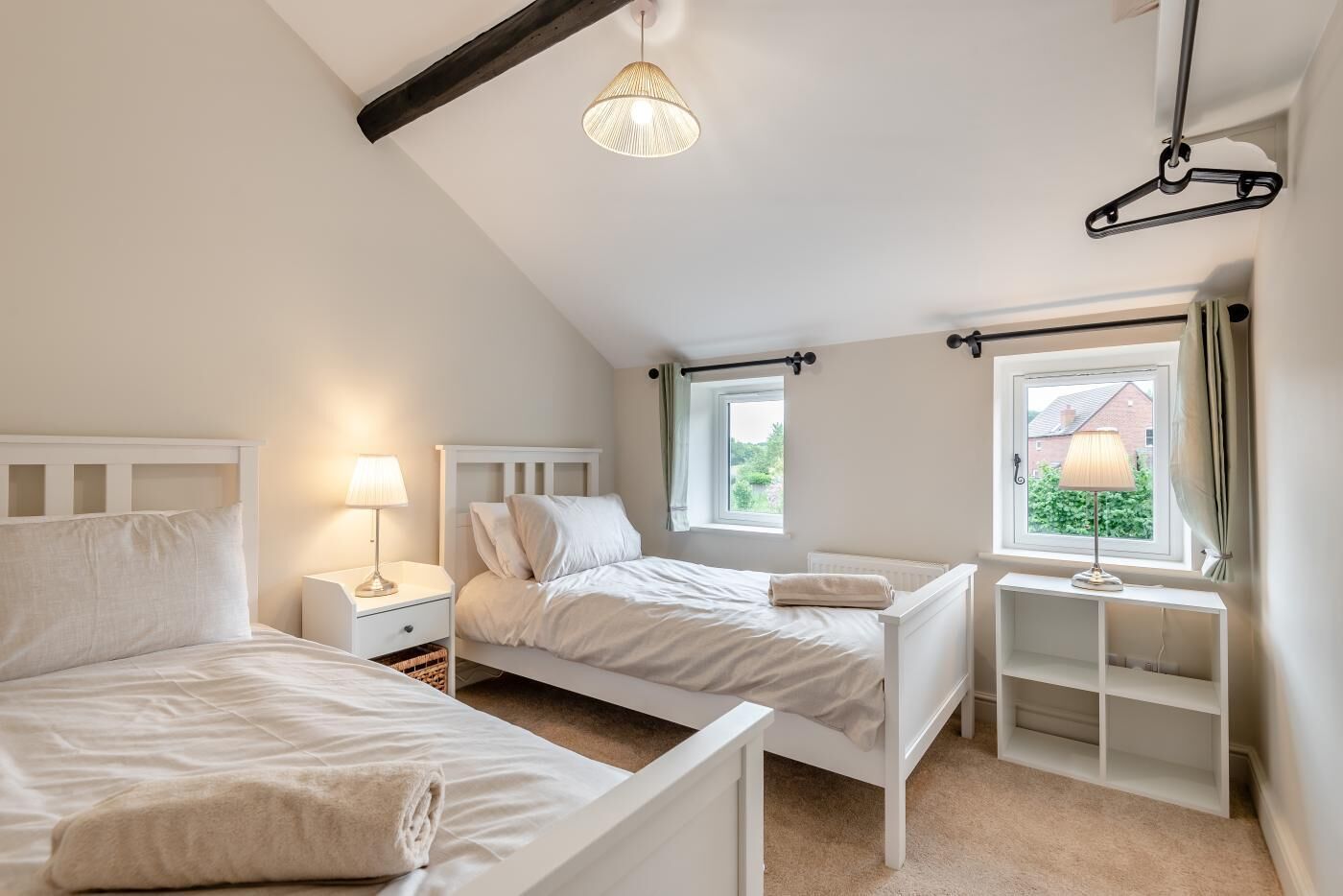Un dormitorio con dos camas, una ventana, una lámpara colgante y una mesita de noche con lámpara.
