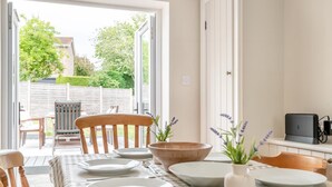 A dining area with a table set for four, a wooden chair, a bowl, and a vase with flowers. - 3 Bed in Alfrick (oc-s32386) (Alfrick)