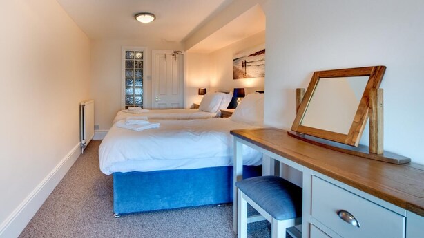 A hotel room with two beds, a desk, a chair, a radiator, a window with a view, and a framed picture on the wall. - 2 Bed in Whitby (oc-w507) (Whitby)