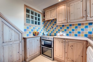 Uma cozinha com armários de madeira, painel de azulejos, fogão e janela.