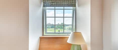 Una habitación con ventana, lámpara, revista y piano.