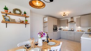 A modern kitchen with white cabinets, a wooden dining table set for two, and a hanging light fixture above the table. - 3 Bed in Whitby (oc-w1001) (Whitby)
