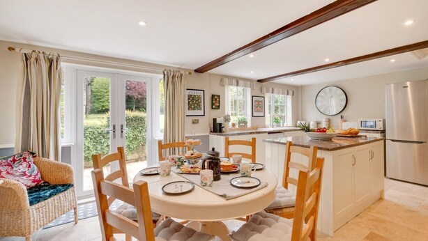 A modern kitchen with a dining area, featuring a round table, chairs, and a view of the garden through large windows. - 4 Bed in Scarborough (oc-sa870) (Scalby)
