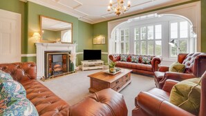 A living room with a fireplace, leather sofas, a television, and a large window with shutters. - 4 Bed in Scarborough (oc-sa870) (Scalby)