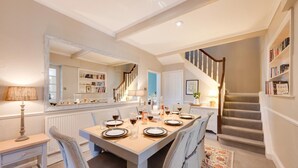 A dining area with a table set for six, a staircase, and a bookshelf with books. - 4 Bed in Scarborough (oc-sa870) (Scalby)