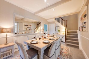 Un coin repas avec une table dressée pour six personnes, un escalier et une bibliothèque remplie de livres.