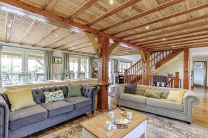 A spacious living area with high ceilings, wooden beams, two sofas, a coffee table, and a dining area with a table set for four.