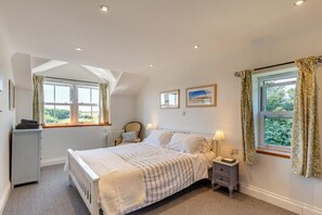 Ein Schlafzimmer mit Bett, Nachttischen, Heizkörper und einem Vorhangfenster.