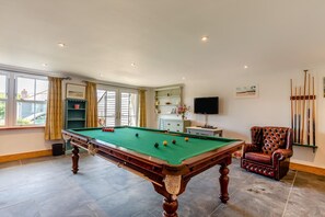 Une table de billard avec des billes, un téléviseur et une chaise dans une pièce dotée d’une fenêtre et d’étagères.