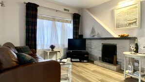 A living room with a brown leather sofa, a flat-screen TV, a fireplace, and a painting of a boat on the wall. - 2 Bed in Whitby (oc-w985) (Whitby)