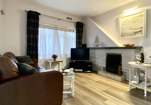 A living room with a brown leather sofa, a flat-screen TV, a fireplace, and a painting of a boat on the wall. - 2 Bed in Whitby (oc-w985) (Whitby)