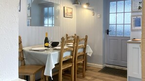 A dining area with a table set for four, a bottle of wine, and a clock on the wall. - 2 Bed in Whitby (oc-w985) (Whitby)