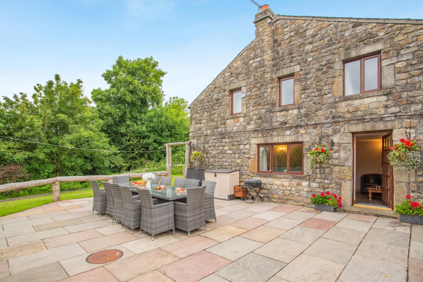 A stone building with a patio area featuring wicker furniture and a grill.