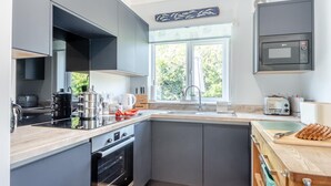 Ett modernt kök med gråa skåp, en inbyggd ugn, en mikrovågsugn och ett fönster som släpper in naturligt ljus.