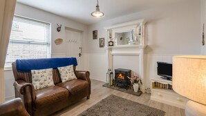 A living room with a fireplace, a leather sofa, a television, and a bookshelf. - 2 Bed in Whitby (oc-w970b) (Whitby)