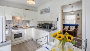 A modern kitchen with white cabinets, a gas stove, a microwave, and a toaster. There is a dining area with a table, chairs, and a vase of sunflowers. - 2 Bed in Whitby (oc-w970b) (Whitby)