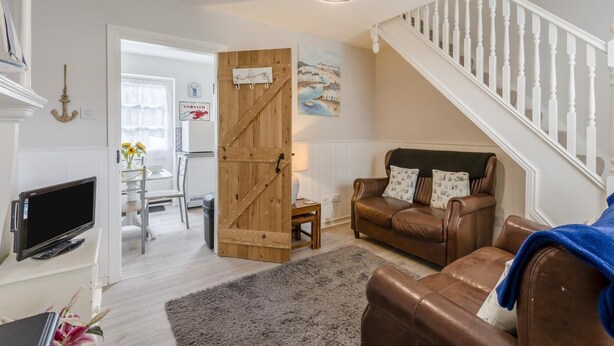 A living room with a brown leather sofa, a television, a wooden door, and a staircase. - 2 Bed in Whitby (oc-w970b) (Whitby)