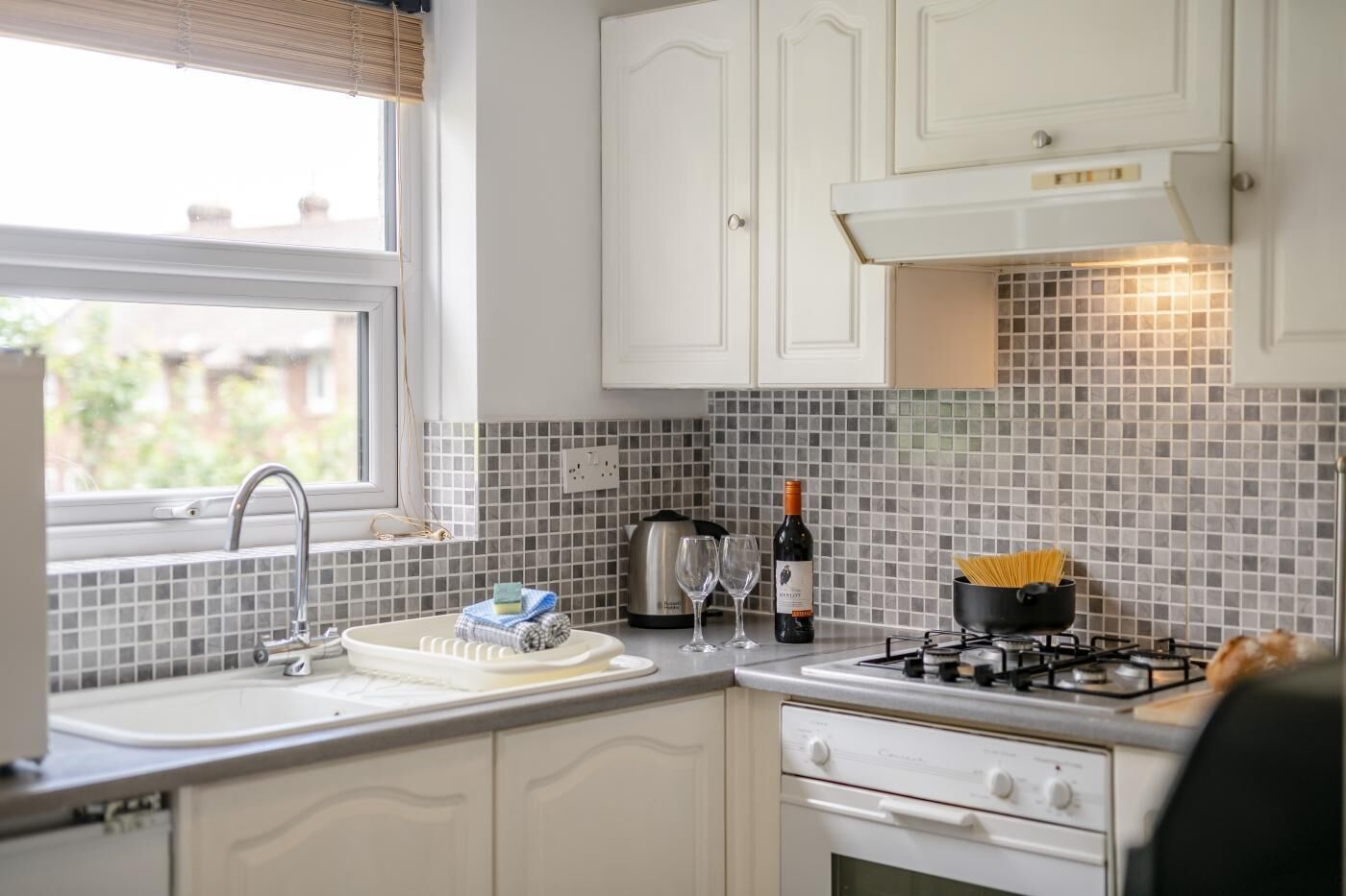 A kitchen with white cabinets, a gas stove, a sink, and a window with blinds.
