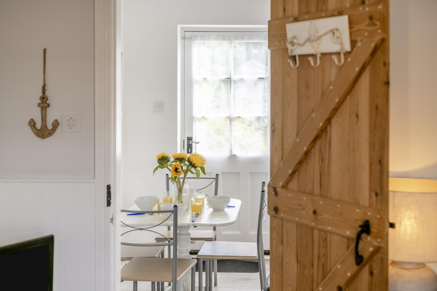 A dining area with a table set for two, a vase with sunflowers, and a wooden door with a coat hanging.