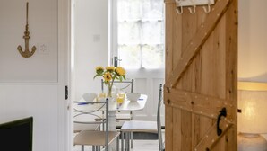A dining area with a table set for two, a vase with sunflowers, and a wooden door with a coat hanging. - 2 Bed in Whitby (oc-w970b) (Whitby)