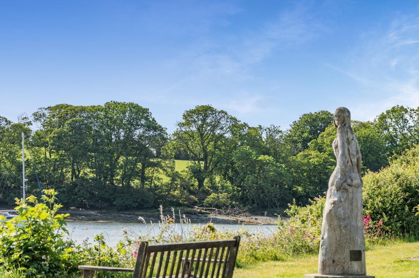 A bench, a statue, and a river with trees in the background.
