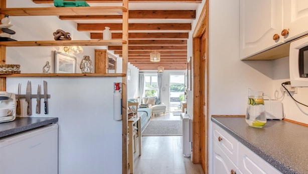 Una cucina con travi in legno, un frigorifero, un lavandino e un piano di lavoro con una caraffa d'acqua.