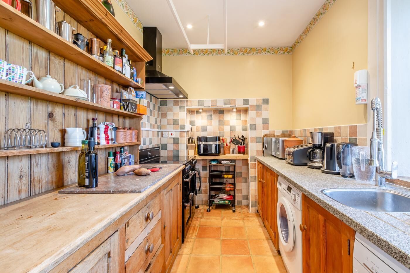 Eine Küche mit Holzausstattung, einem eingebauten Backofen, einer Waschmaschine und einer gefliesten Spritzschutzwand.