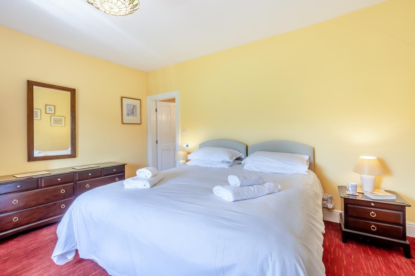 Une chambre d’hôtel avec un grand lit, une commode, une table de chevet, une lampe et un miroir.