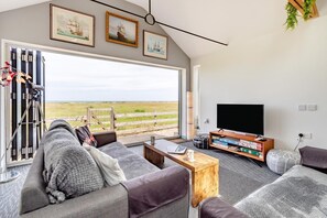 A modern living room with a large window, a flat-screen TV, and a cozy seating area. - 2 Bed in Walcott (oc-s32403) (Walcott)