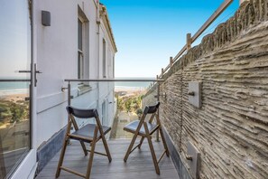 En balkon med to stole, udsigt til stranden og en stenvæg.