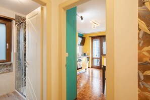Un pasillo que conduce a una cocina con piso de madera, una pared de acento color verde azulado y una puerta de vidrio.