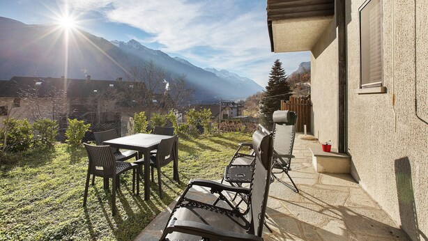 Eine Terrasse mit Tisch und Stühlen, eine hölzerne Bank und eine Bergblick im Hintergrund.