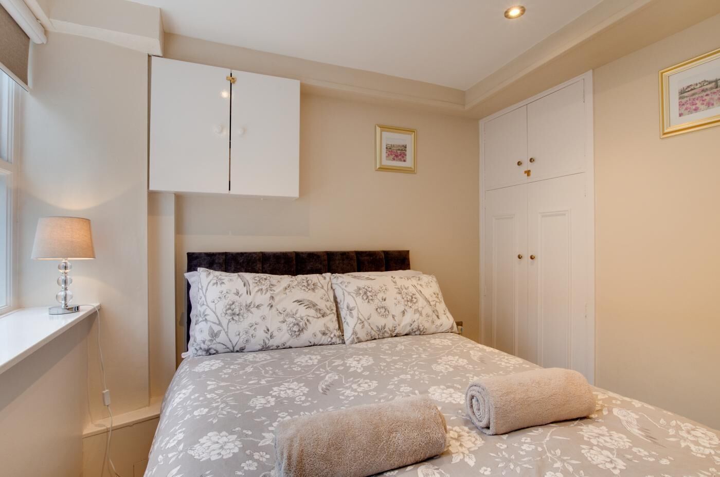 Ein Schlafzimmer mit Bett, Nachttisch, Lampe, Kleiderschrank und einem gerahmten Bild an der Wand.