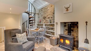 Una sala de estar acogedora con una pared de piedra, una chimenea, un comedor con mesa y sillas, y un sofá gris con un cojín estampado.
