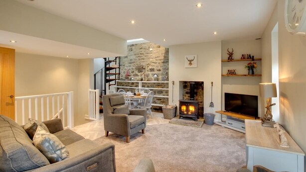 Una sala de estar acogedora con una pared de piedra, una chimenea, un televisor y una escalera que sube a un nivel superior.