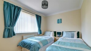 Ein Schlafzimmer mit zwei Betten, einem Fenster mit Vorhängen, einem Heizkörper und einem Wandbild.