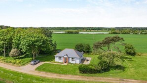 Ein eingeschossiges Haus mit grauem Dach, umgeben von einem grünen Feld und Bäumen.
