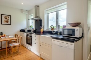 A modern kitchen with a stove, oven, microwave, and dishwasher. There is a dining table with chairs and a window with a view.