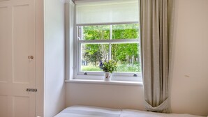 Ein Zimmer mit einem Bett, einem Fenster mit Blick ins Grüne und einer Tür.