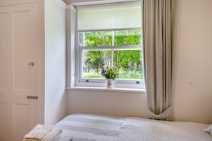A room with a bed, a window with a view of greenery, and a door.