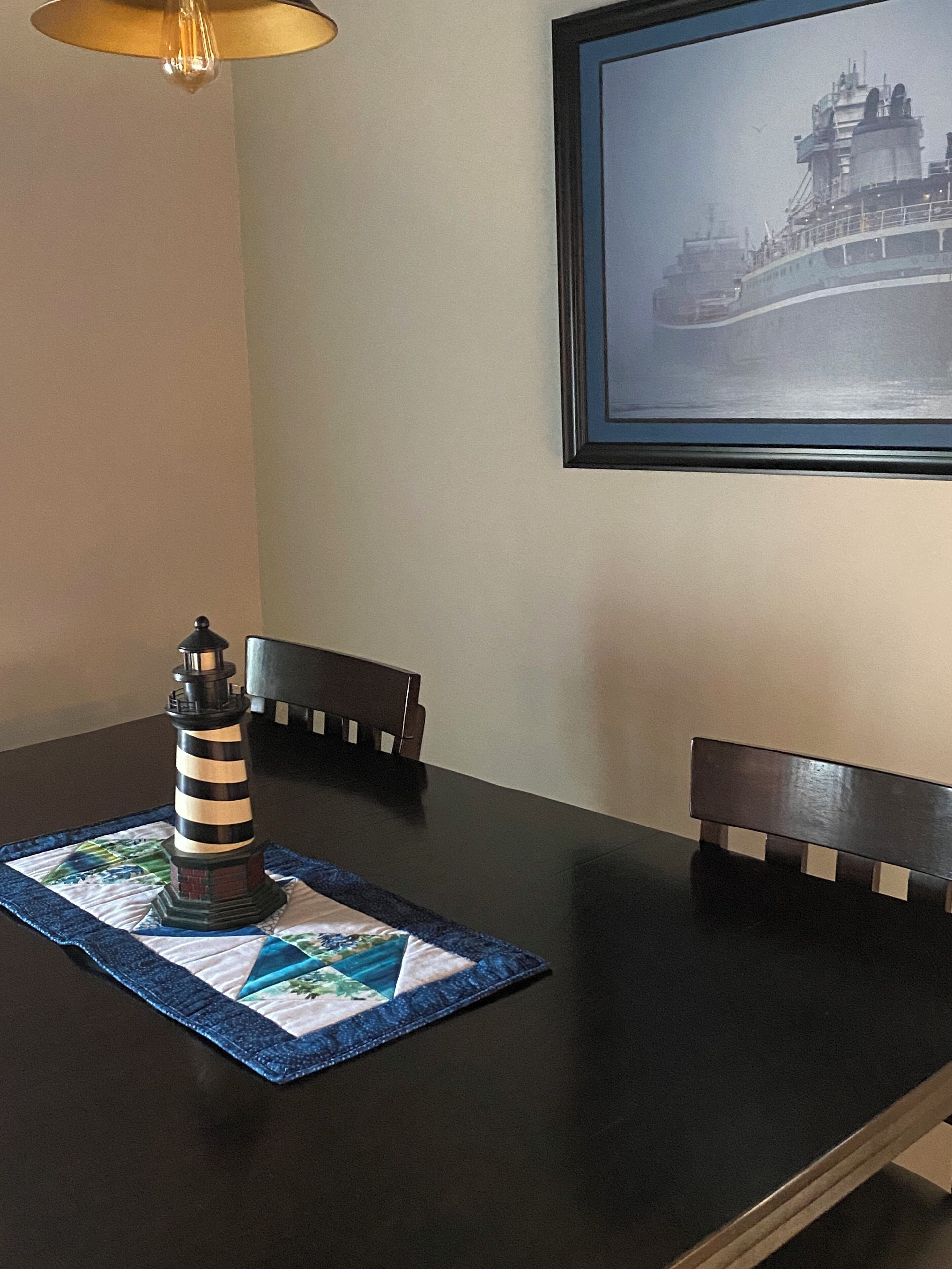 A dining table with a black tablecloth, a lighthouse-shaped centerpiece, and a framed picture on the wall.