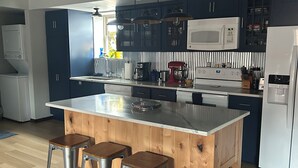 A modern kitchen with a central island, bar stools, dark cabinets, and a white refrigerator.