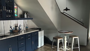 A modern kitchen with dark blue cabinets, a white refrigerator, and a wooden dining table with two stools.