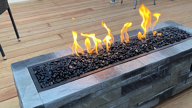 A deck with a stone fire feature, metal chairs, and a wooden railing.