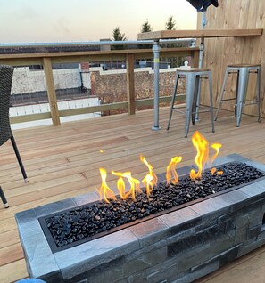 A deck with a stone fire feature, metal chairs, and a wooden railing. - Harbor Rail Loft: an upscale retreat, three bedrooms, two baths, sauna, and deck (Two Harbors)