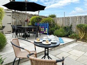 En terrasse med udendørs møbler, et bord dækket med tallerkener og teskeer, samt en blå legekonstruktion.