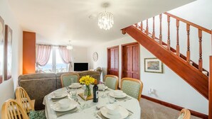 Un coin repas avec une table ronde dressée pour quatre personnes, un lustre et un escalier en bois.